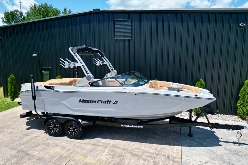 Slide: The Image of 2026 MasterCraft XT24 boat on trailer, parked outdoors near a black building. - 25