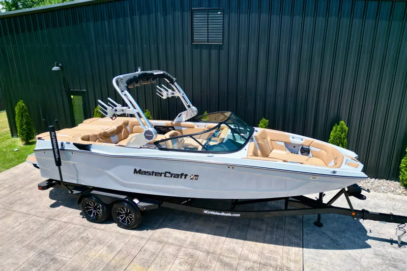 Slide: The Image of 2026 MasterCraft XT24 boat on trailer, parked outdoors, featuring sleek design and tan interior. - 20