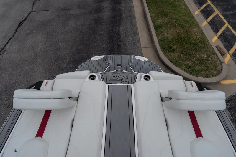 Slide: The Image of 2023 MasterCraft XT24 boat interior with white seats and red accents, parked on pavement. - 37