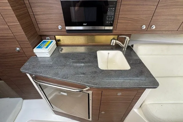 Slide: The Image of 2023 Boston Whaler 325 Conquest galley with sink, microwave, and compact refrigerator. - 45
