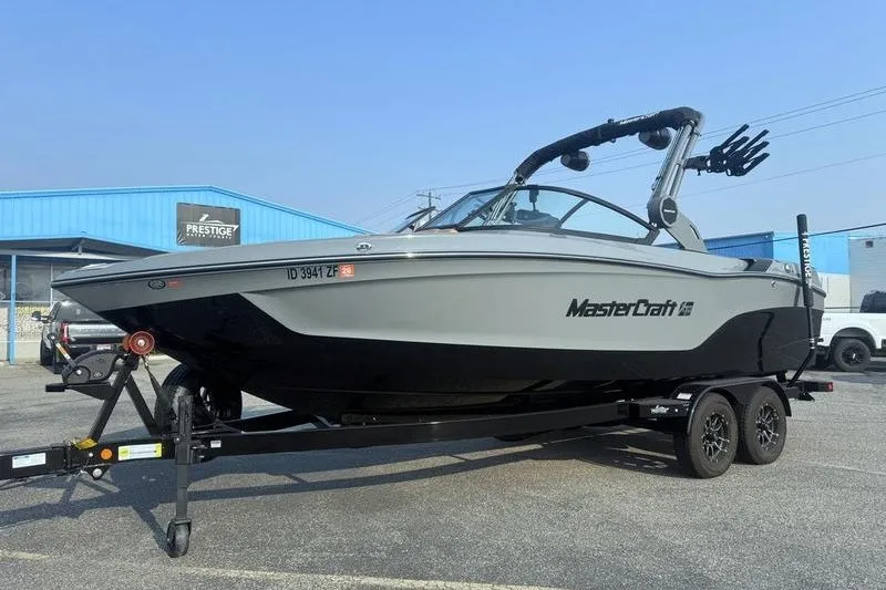 Slide: The Image of 2026 MasterCraft XT23 boat on trailer, parked outside a blue building. - 2