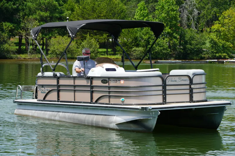 The Image of 2024 Lexington Palm Breeze Emerg pontoon boat cruising on a serene lake. - 1