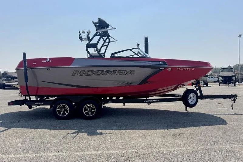 Slide: The Image of 2020 Moomba Max boat in red and gray on a trailer in a parking lot. - 2