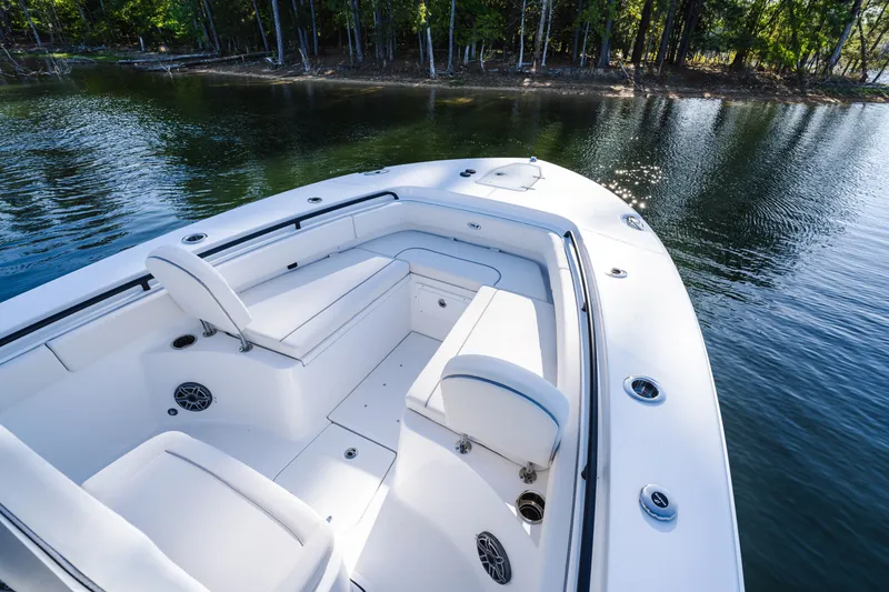 Slide: The Image of 2027 Sea Hunt Ultra 265SE boat interior with white seating, on calm water near forested shore. - 24