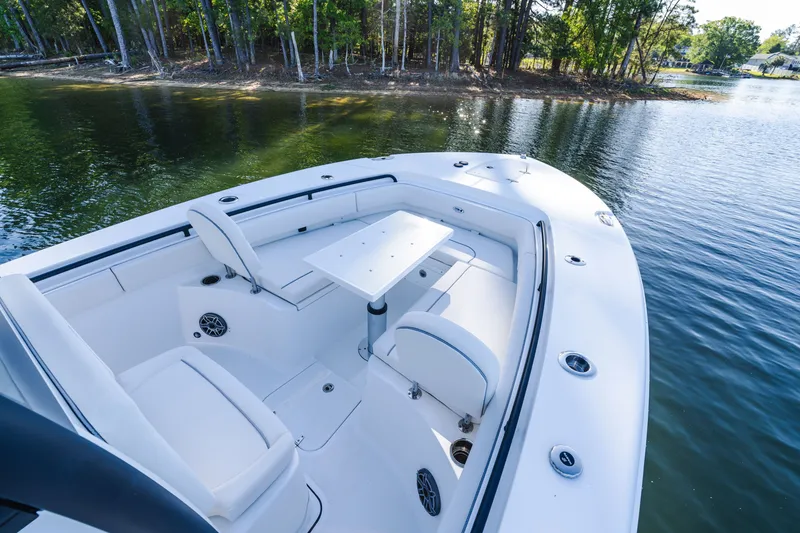 Slide: The Image of 2027 Sea Hunt Ultra 265SE boat interior with seating and table, near a serene lakeside. - 26