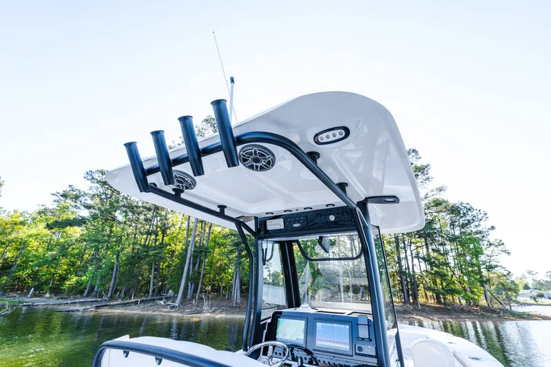 Slide: The Image of 2027 Sea Hunt Ultra 265SE boat console with rod holders and electronics, near a wooded shoreline. - 23