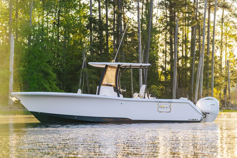 Slide: The Image of 2027 Sea Hunt Ultra 265SE boat on tranquil water, surrounded by lush trees. - 60