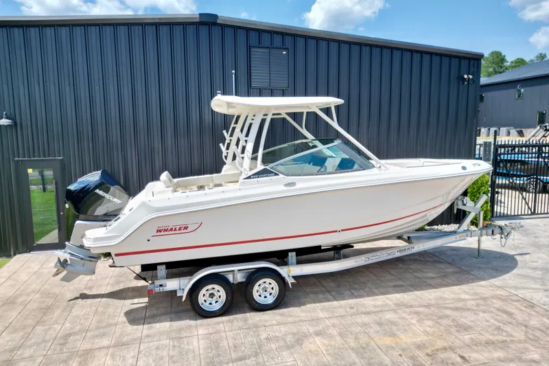 Slide: The Image of 2025 Boston Whaler 240 Vantage boat on trailer, parked outside a modern building. - 5