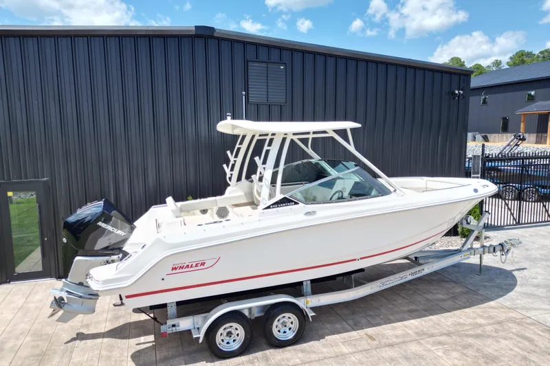 Slide: The Image of 2025 Boston Whaler 240 Vantage boat on trailer, parked outdoors near a black building. - 16