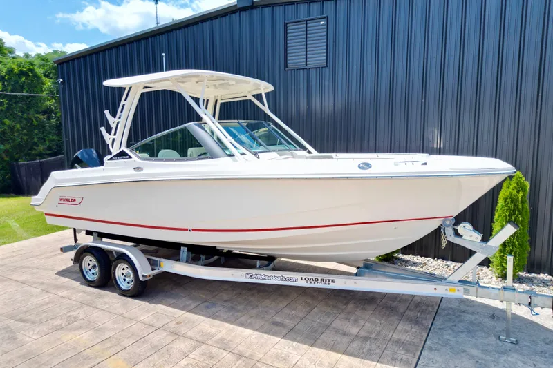 Slide: The Image of 2025 Boston Whaler 240 Vantage boat on trailer, parked outdoors near a metal building. - 6