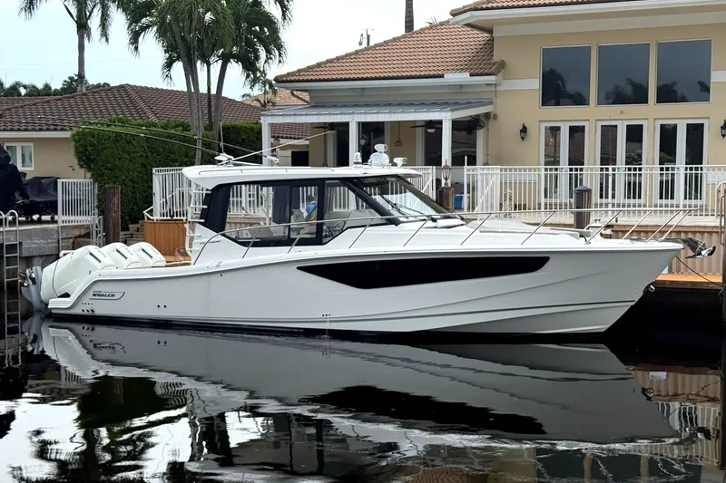 The Image of A sleek, modern boat docked in front of a large house with palm trees in the background. - 1
