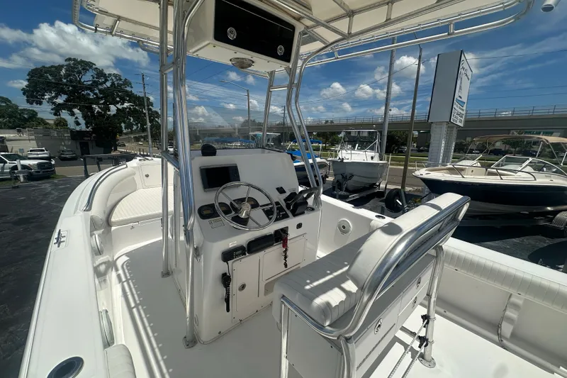 Slide: The Image of 2005 Cobia 254 Center Console boat with steering wheel and seating, docked under a sunny sky. - 18