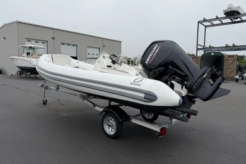 Slide: The Image of 2024 Zodiac Yachtline 490 boat with Mercury engine on trailer, parked outside a warehouse. - 2