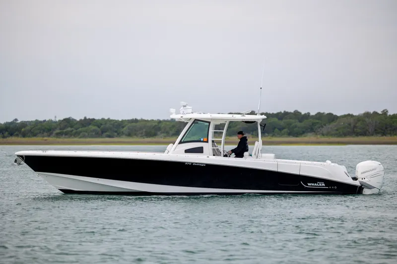 Slide: The Image of 2017 Boston Whaler 370 Outrage boat cruising on calm water near a forested shoreline. - 2