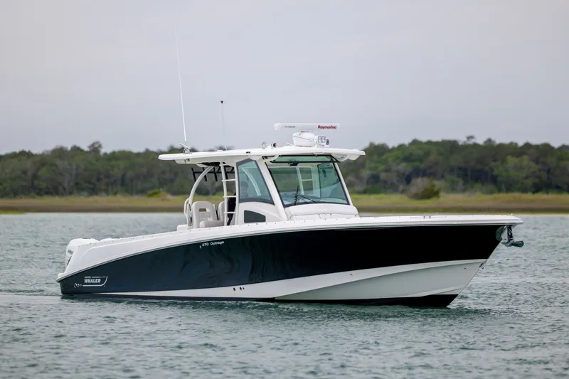Slide: The Image of 2017 Boston Whaler 370 Outrage boat on calm water, with lush greenery in the background. - 10