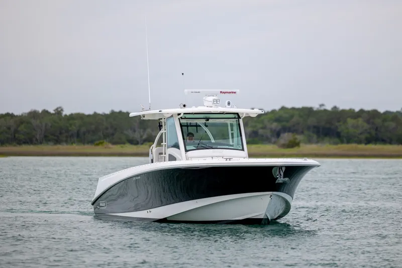 Slide: The Image of 2017 Boston Whaler 370 Outrage boat cruising on calm waters near a forested shoreline. - 11