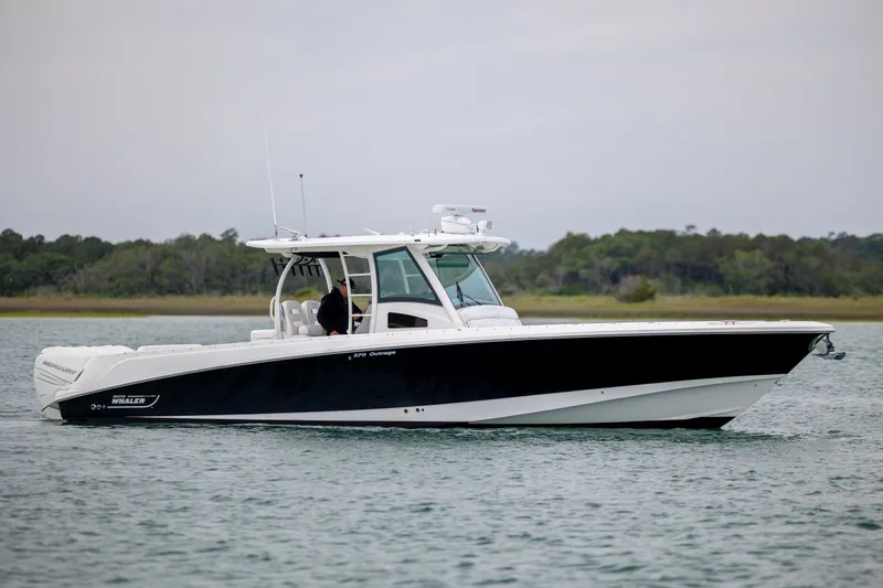 Slide: The Image of 2017 Boston Whaler 370 Outrage boat cruising on calm water near a forested shoreline. - 9