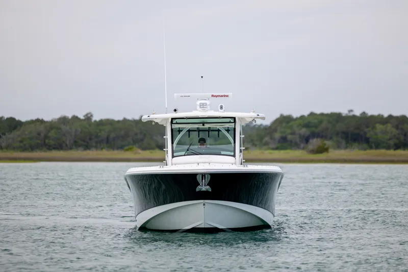 Slide: The Image of 2017 Boston Whaler 370 Outrage boat on water, front view with forested background. - 12