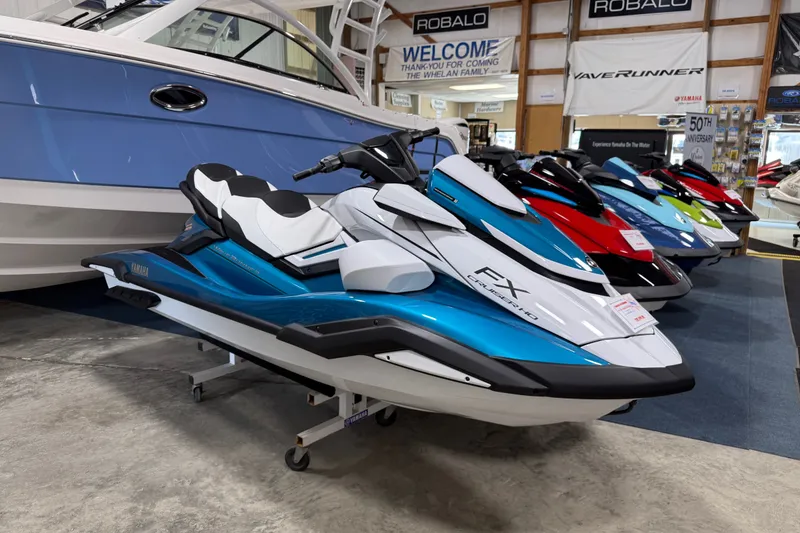 The Image of 2026 Yamaha WaveRunner FX Cruiser HO in showroom, blue and white design, displayed alongside other models. - 0