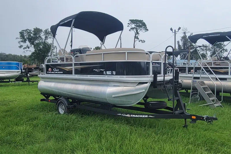 The Image of 2024 Sun Tracker Party Barge 16 DLX pontoon boat on trailer, parked on grass. - 0