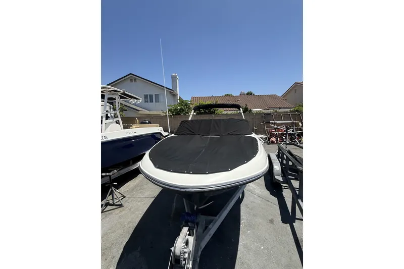 Slide: The Image of 2023 Bayliner VR4 Bowrider I/O boat with cover, parked on a trailer in a residential area. - 3