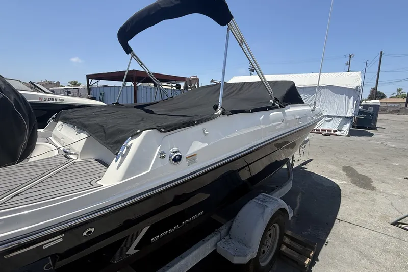 Slide: The Image of 2023 Bayliner VR4 Bowrider I/O boat with black cover on trailer, outdoor setting. - 4