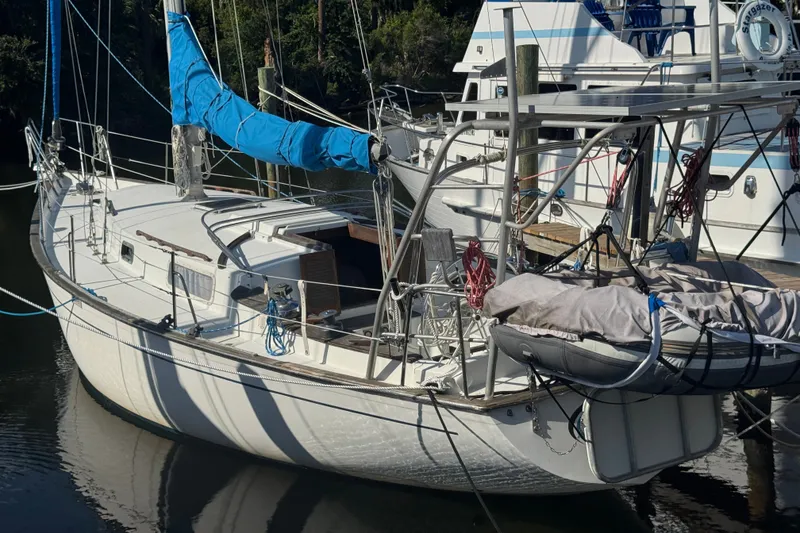 The Image of 1980 Morgan 382 sailboat docked, featuring blue sail cover and dinghy on deck. - 0