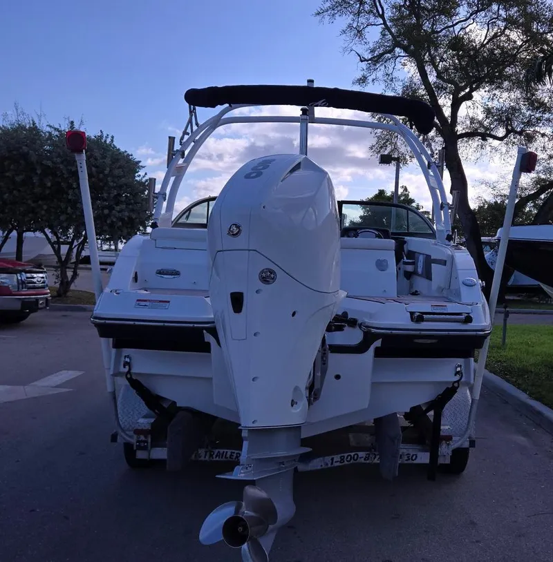 Slide: The Image of 2023 Monterey M225 boat with outboard motor, parked outdoors, surrounded by trees. - 1