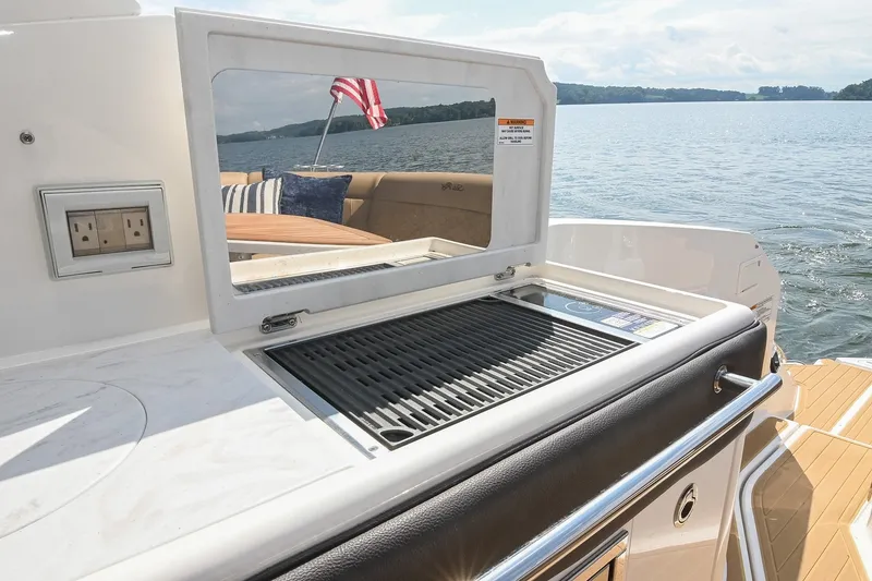 Slide: The Image of 2024 Sea Ray Sundancer 320 boat grill area with scenic lake view. - 40