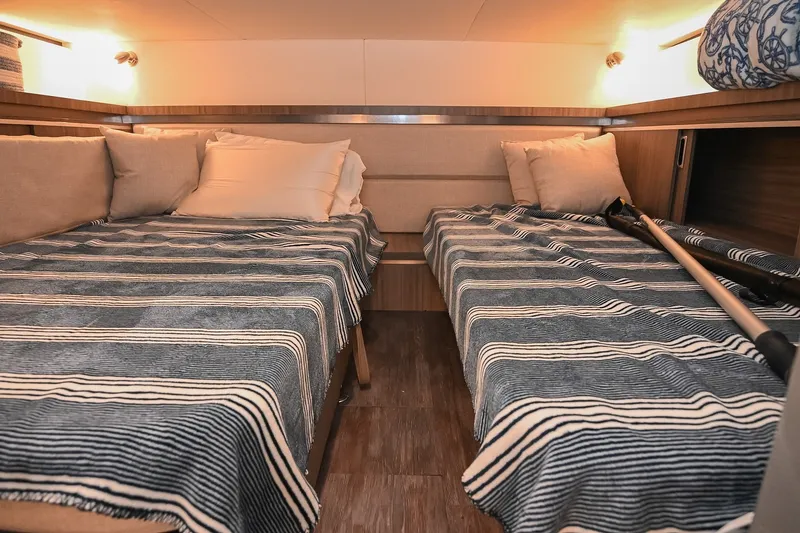 Slide: The Image of 2024 Sea Ray Sundancer 320 cabin with twin beds, striped bedding, and cozy lighting. - 65