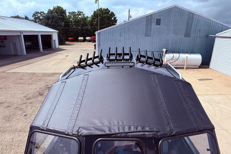 Slide: The Image of Roof view of 2026 Lund 210 Heavy Gauge boat with rod holders, parked near metal buildings. - 27
