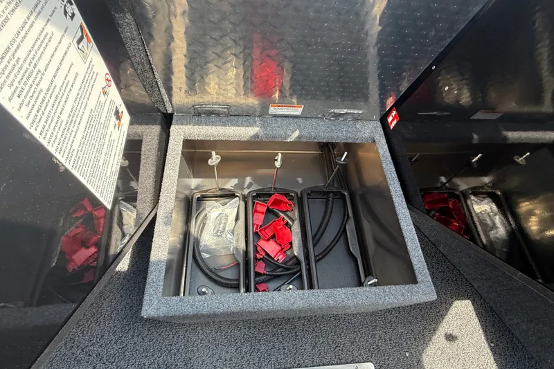 Slide: The Image of Open storage compartment in 2026 Lund 210 Heavy Gauge boat, featuring cables and red connectors. - 22