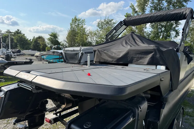 Slide: The Image of 2024 Manitou Explore Dual Engine boat with covered deck, parked outdoors under a clear sky. - 5