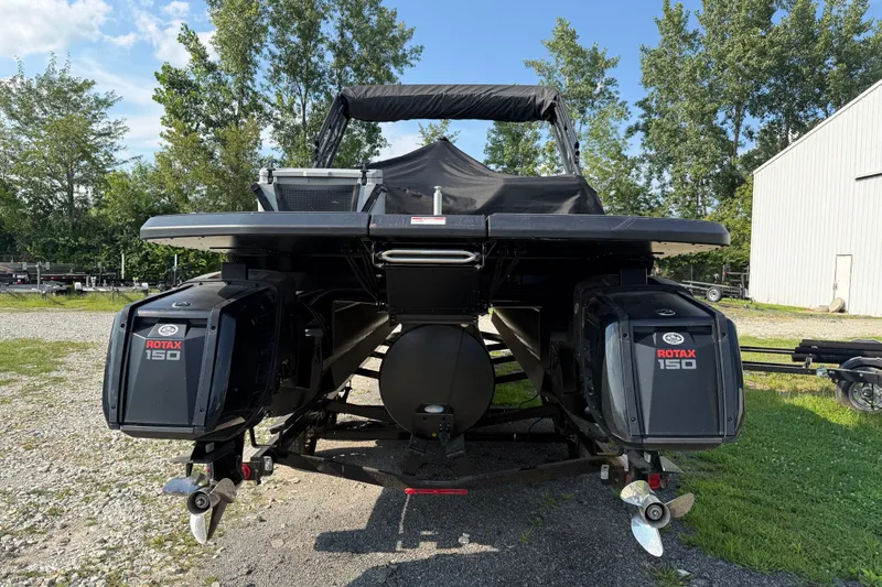 Slide: The Image of 2024 Manitou Explore Dual Engine boat with Rotax 150 engines, parked outdoors. - 3