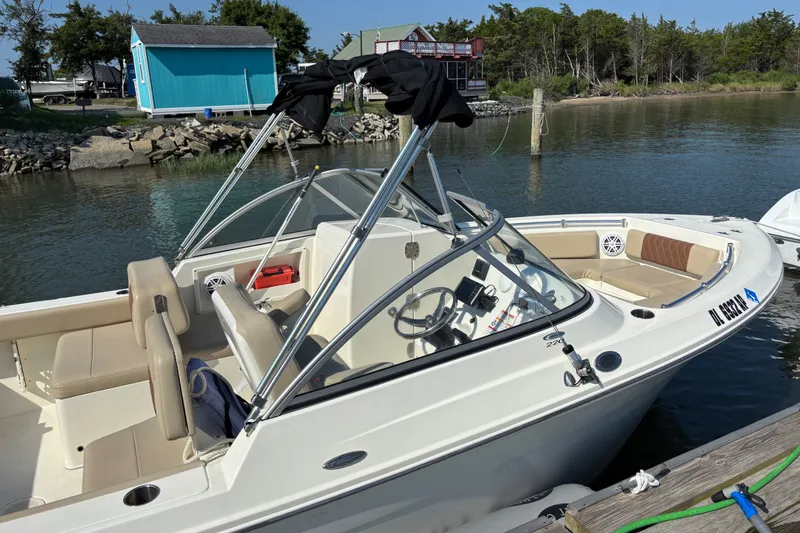 Slide: The Image of 2024 Cobia 220 Dual Console boat docked by a scenic waterfront. - 3