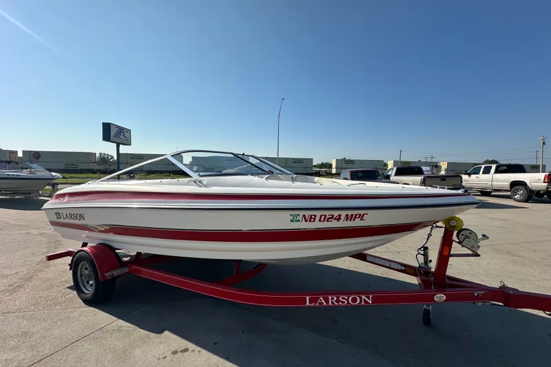 Slide: The Image of 2004 Larson SEi 190 boat on red trailer in parking lot under clear blue sky. - 1
