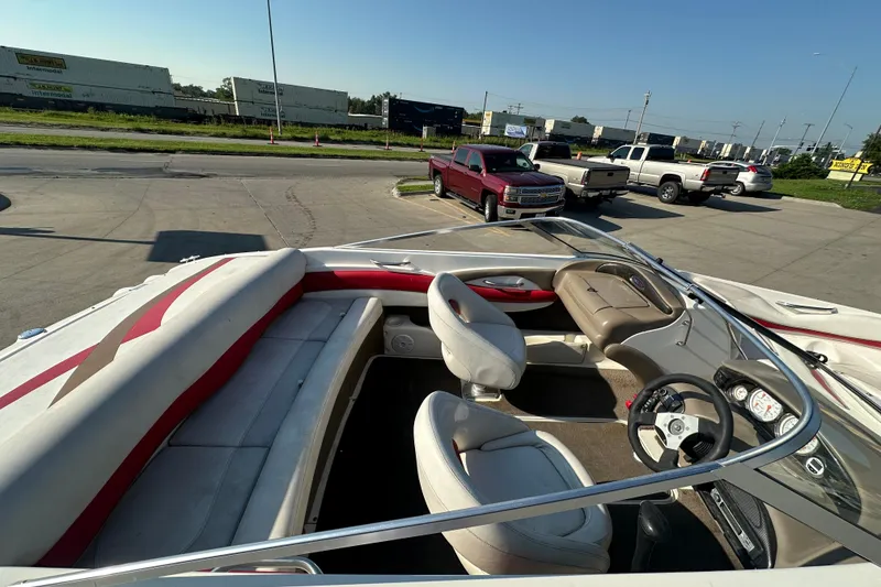 Slide: The Image of 2004 Larson SEi 190 boat interior with red and white seating, parked near trucks. - 9