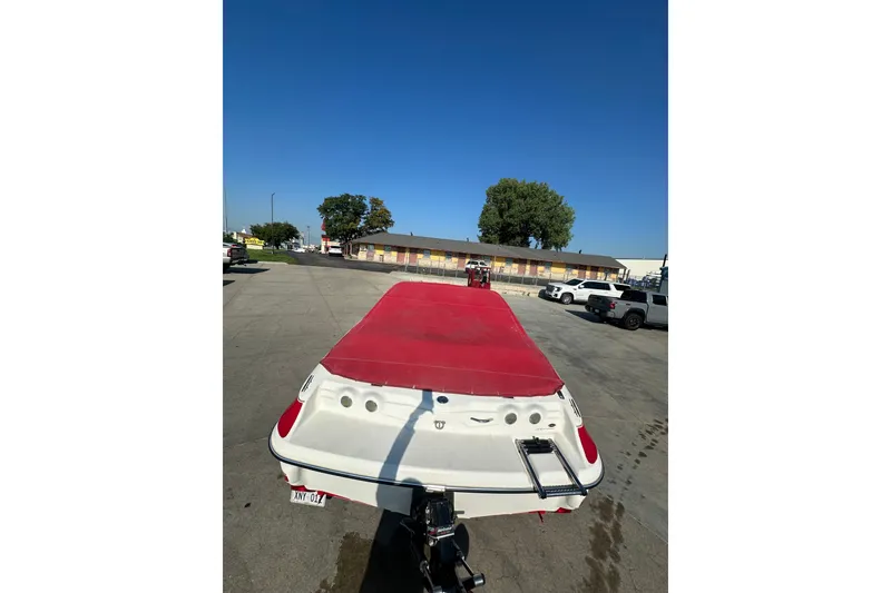 Slide: The Image of 2004 Larson SEi 190 boat with red cover in parking lot under clear blue sky. - 5