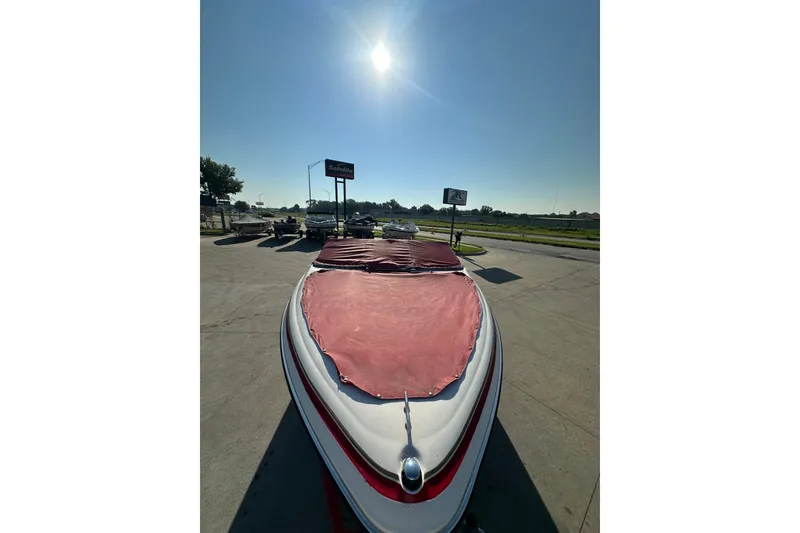 Slide: The Image of 2004 Larson SEi 190 boat with red cover, parked under a bright sun. - 6