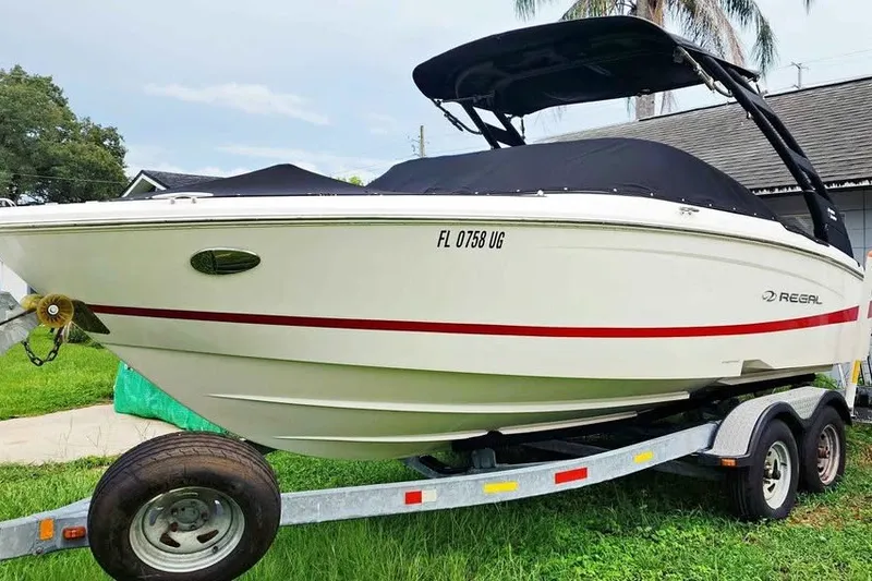 The Image of 2022 Regal LS2 boat on trailer, white with red stripe, covered and parked outdoors. - 0
