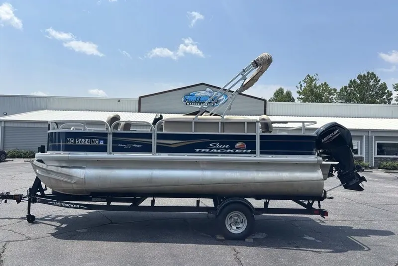 The Image of 2024 Sun Tracker Bass Buggy 18 DLX pontoon boat on trailer, parked outdoors. - 1