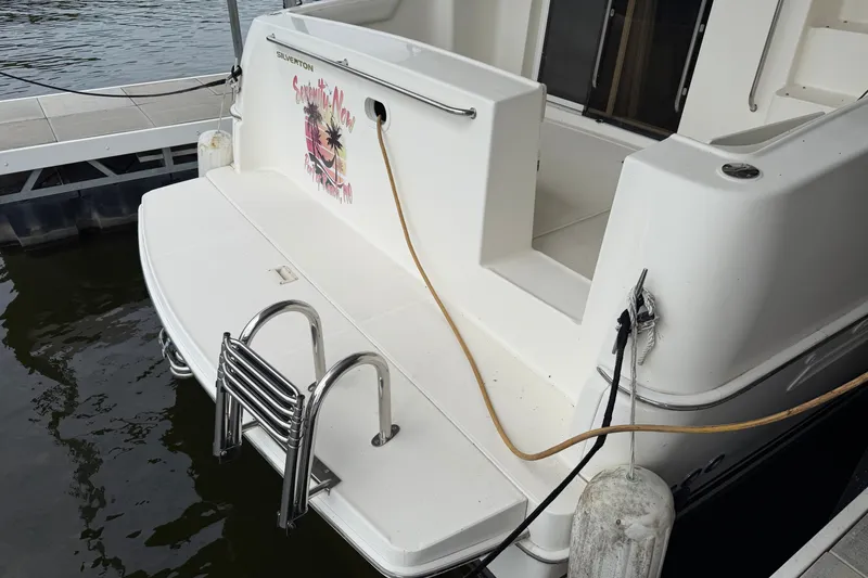 Slide: The Image of 2002 Silverton 330 Sport Bridge boat docked, featuring a swim platform and ladder. - 7