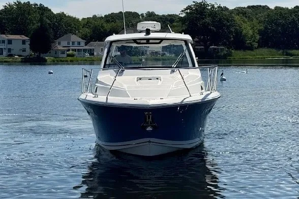 Slide: The Image of 2021 Pursuit OS 325 Offshore boat on a serene lake with houses in the background. - 6