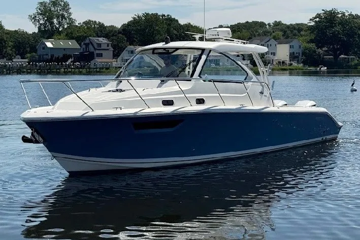Slide: The Image of 2021 Pursuit OS 325 Offshore boat on calm water, surrounded by houses and trees. - 5