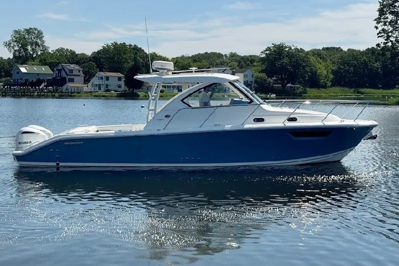 The Image of 2021 Pursuit OS 325 Offshore boat on calm water, surrounded by greenery and houses. - 0
