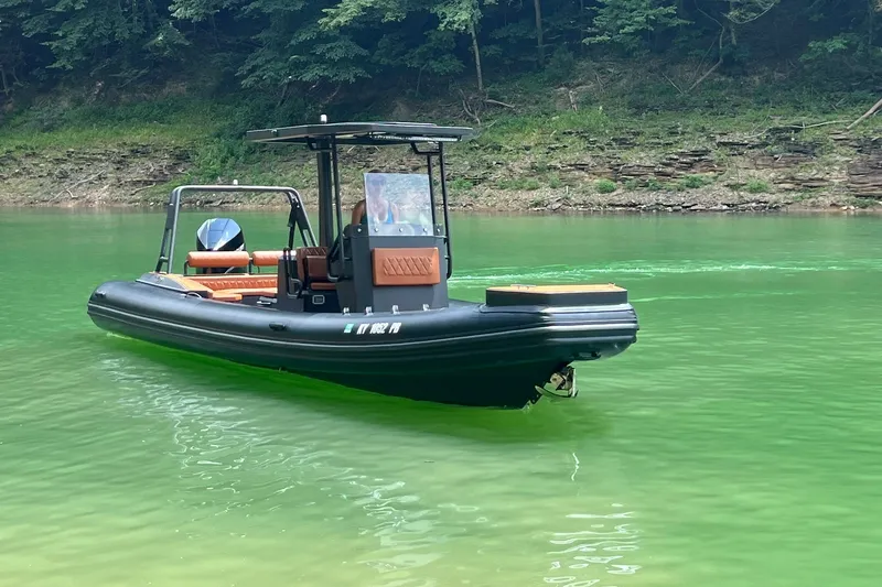 The Image of 2026 Patrol 760 RIB boat on vibrant green water near forested shoreline. - 0