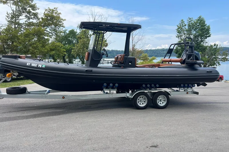 Slide: The Image of 2026 Patrol 760 RIB boat on trailer by a lakeside, surrounded by trees. - 22