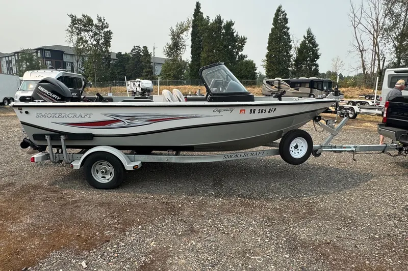 Slide: The Image of 2016 SMOKERCRAFT Osprey boat on trailer, parked outdoors with trees in background. - 2