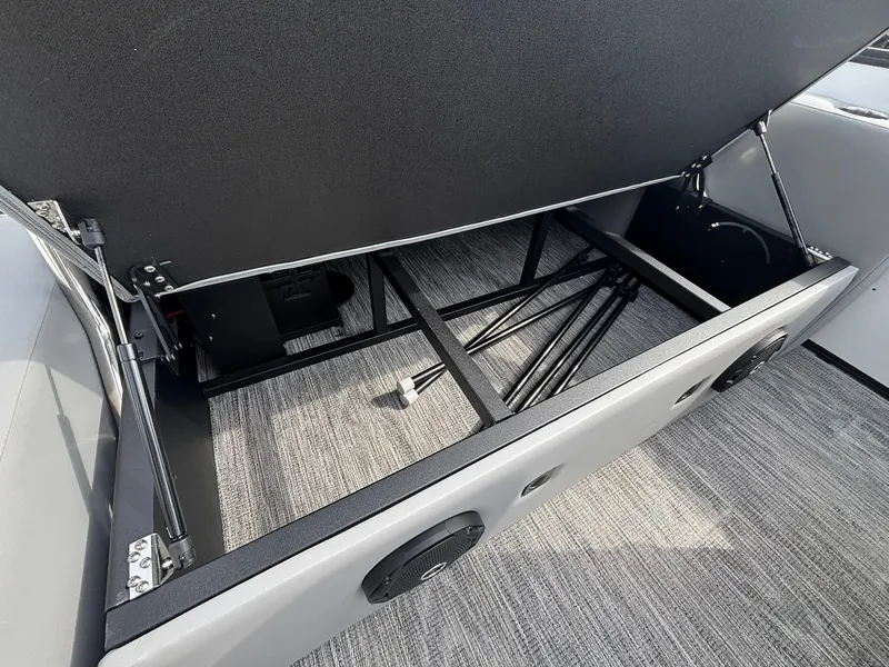 Slide: The Image of An open storage compartment on a Bentley Pontoons 200 Legacy Swingback boat reveals metal framing and gray carpeting. - 26