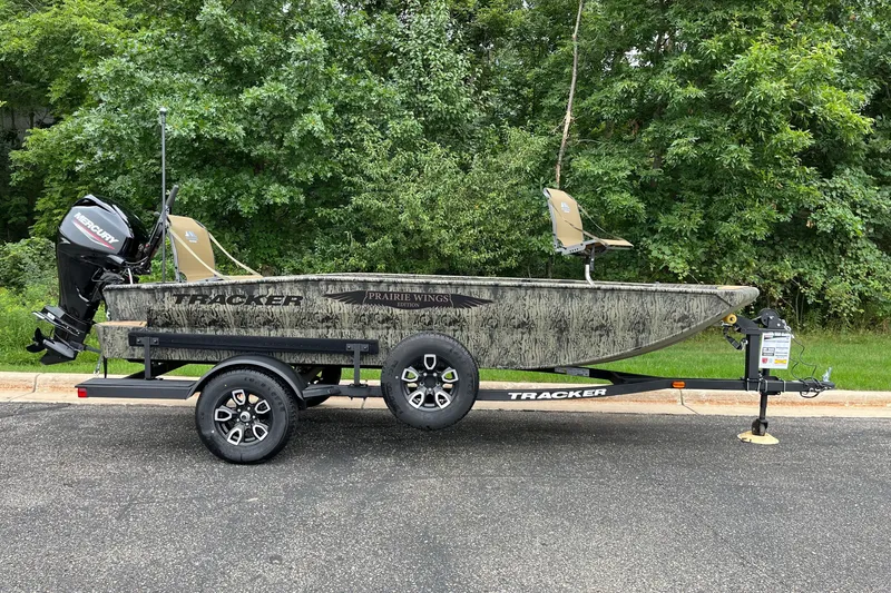 The Image of 2026 Tracker Grizzly 1650 T Prairie Wings Edition boat on trailer, parked by lush greenery. - 0